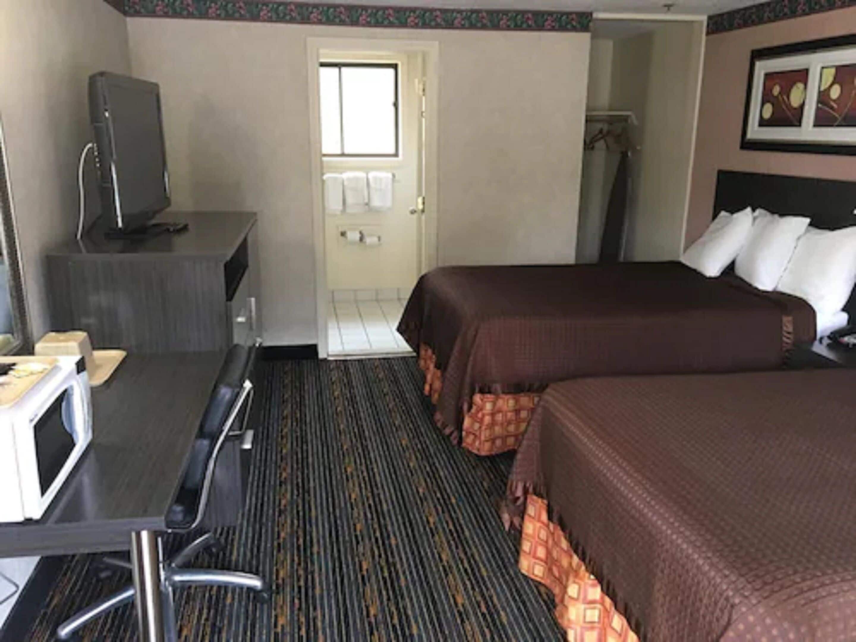 A hotel room with a bed, a desk with a computer, a television, and a shower area.