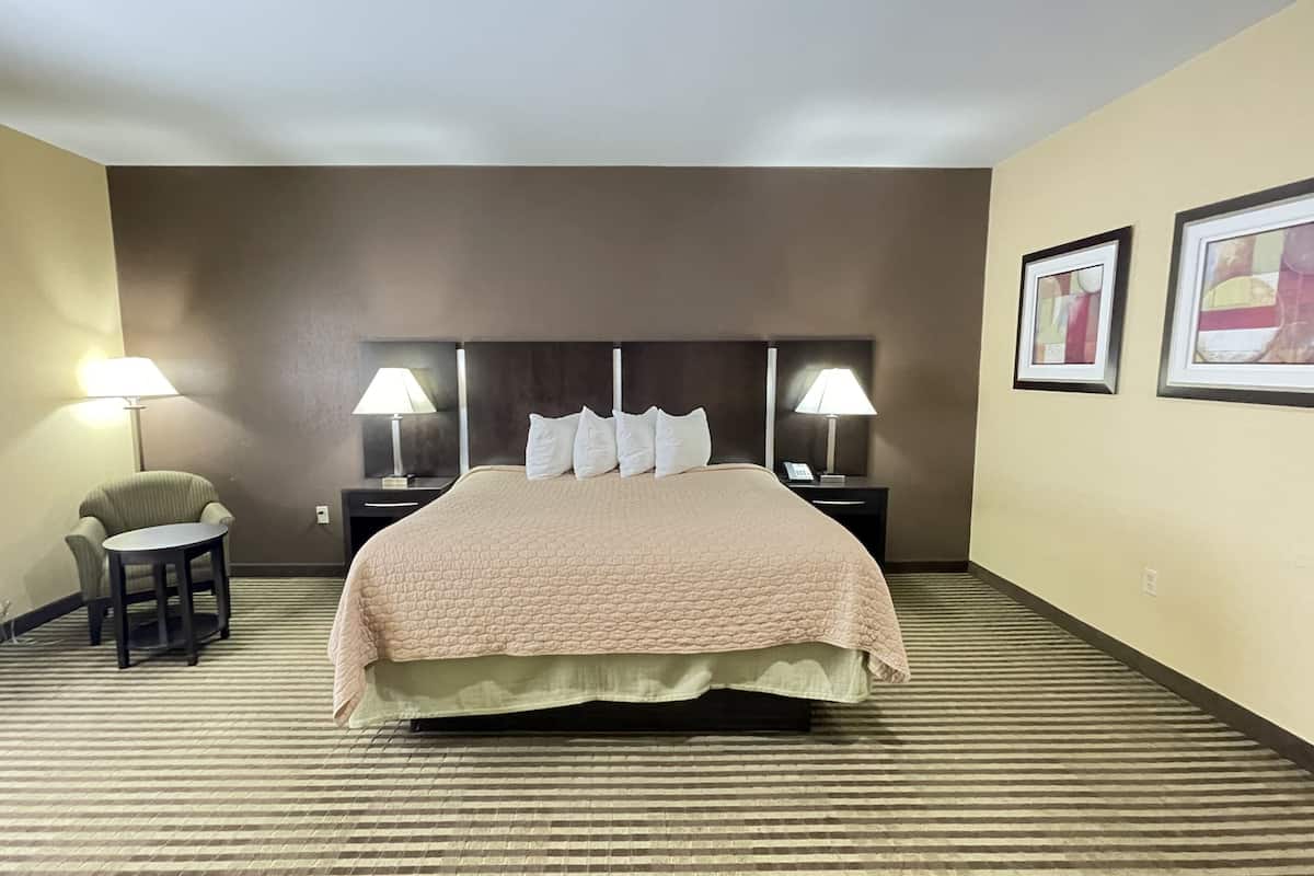 A hotel room with a large bed, two bedside tables with lamps, a small armchair, and a carpeted floor.
