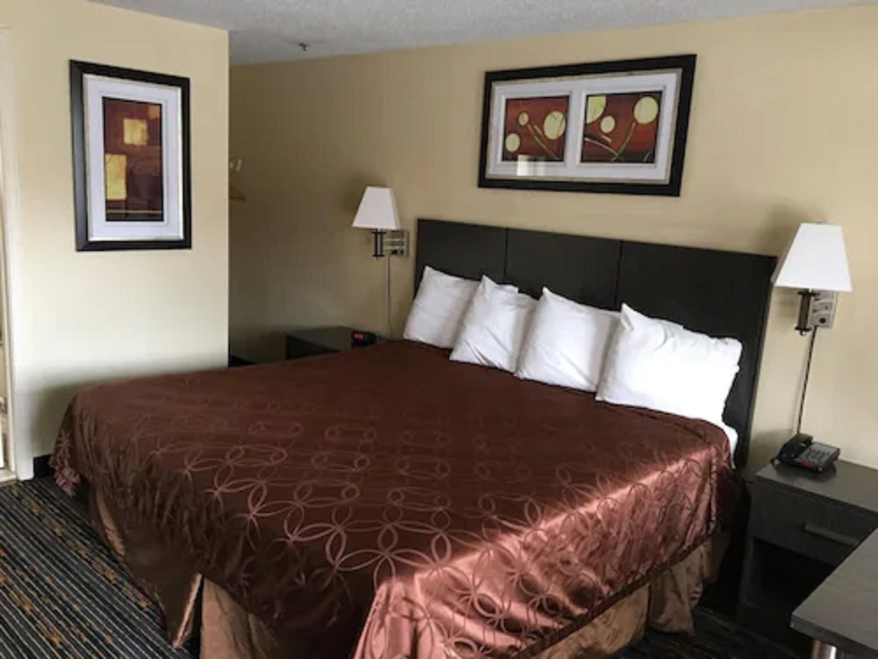 Une chambre d’hôtel avec un grand lit, deux tables de chevet avec des lampes et deux tableaux encadrés accrochés aux murs.