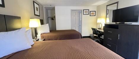 A hotel room with two beds, a desk with a chair, a television, and a wardrobe.