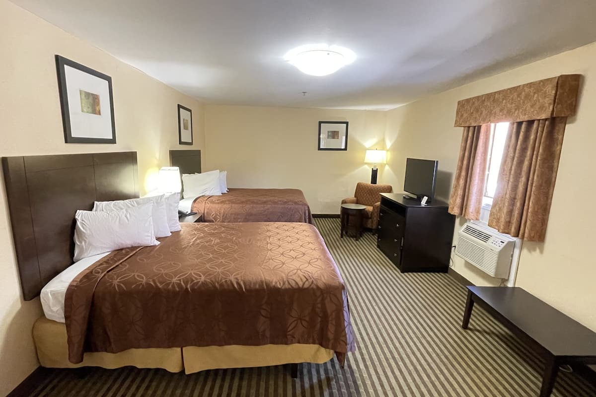 A hotel room with two beds, a desk, a chair, a TV, and a window with curtains.