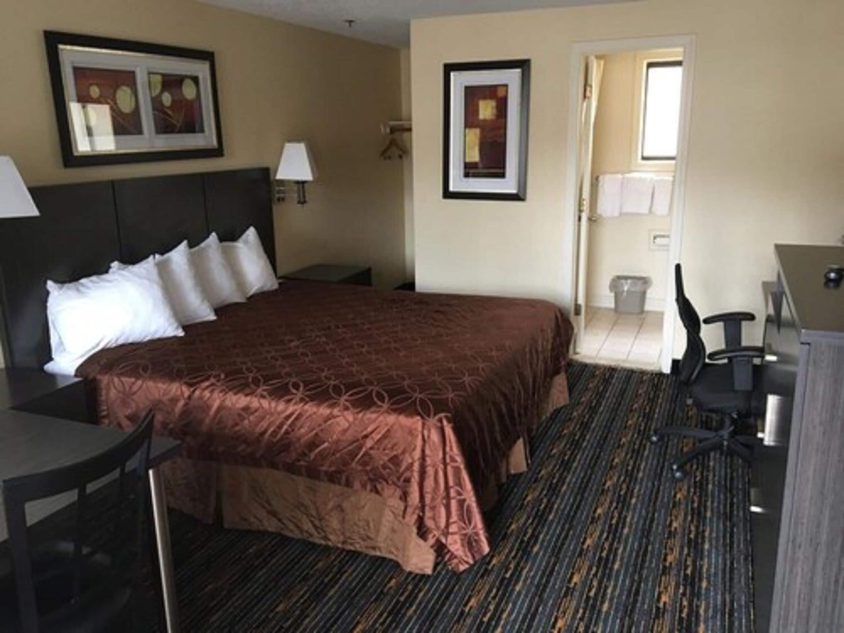 A hotel room with a large bed, a desk, a chair, and a small table. There are two framed pictures on the wall.