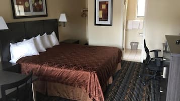 A hotel room with a large bed, a desk, a chair, and a small table. There are two framed pictures on the wall.