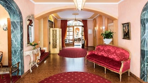 A grand hallway with marble walls, a red carpet, and a red sofa. - Romantik Hotel Bülow Residenz (Dresden)