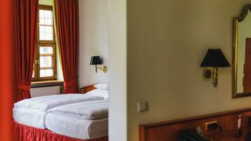 A hotel room with a bed, a window with red curtains, a lamp, and a mirror.