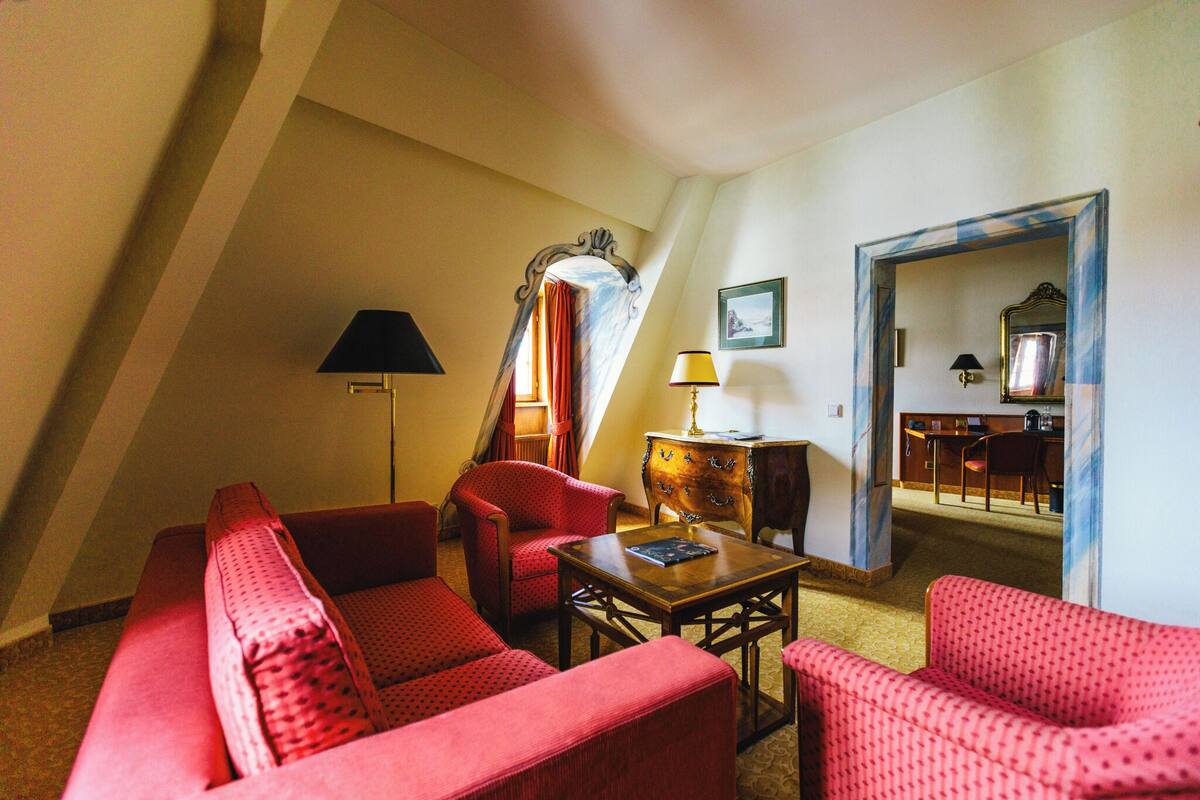 A room with a sloped ceiling, red upholstered furniture, a wooden table, and a mirror.
