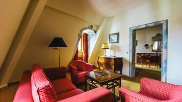 A room with a sloped ceiling, red upholstered furniture, a wooden table, and a mirror.
