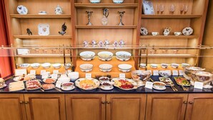 A buffet with various dishes and a display of porcelain items on shelves. - Romantik Hotel Bülow Residenz (Dresden)