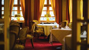 A dining area with tables set for service, chairs, and a window with curtains.