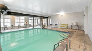 Una piscina interior con agua cristalina, rodeada de sillas y mesas, y amplias ventanas que proporcionan luz natural.