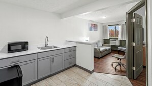 Una cocina moderna con armarios grises, un microondas y un lavabo. Hay una pequeña zona de estar con un sofá y una silla.