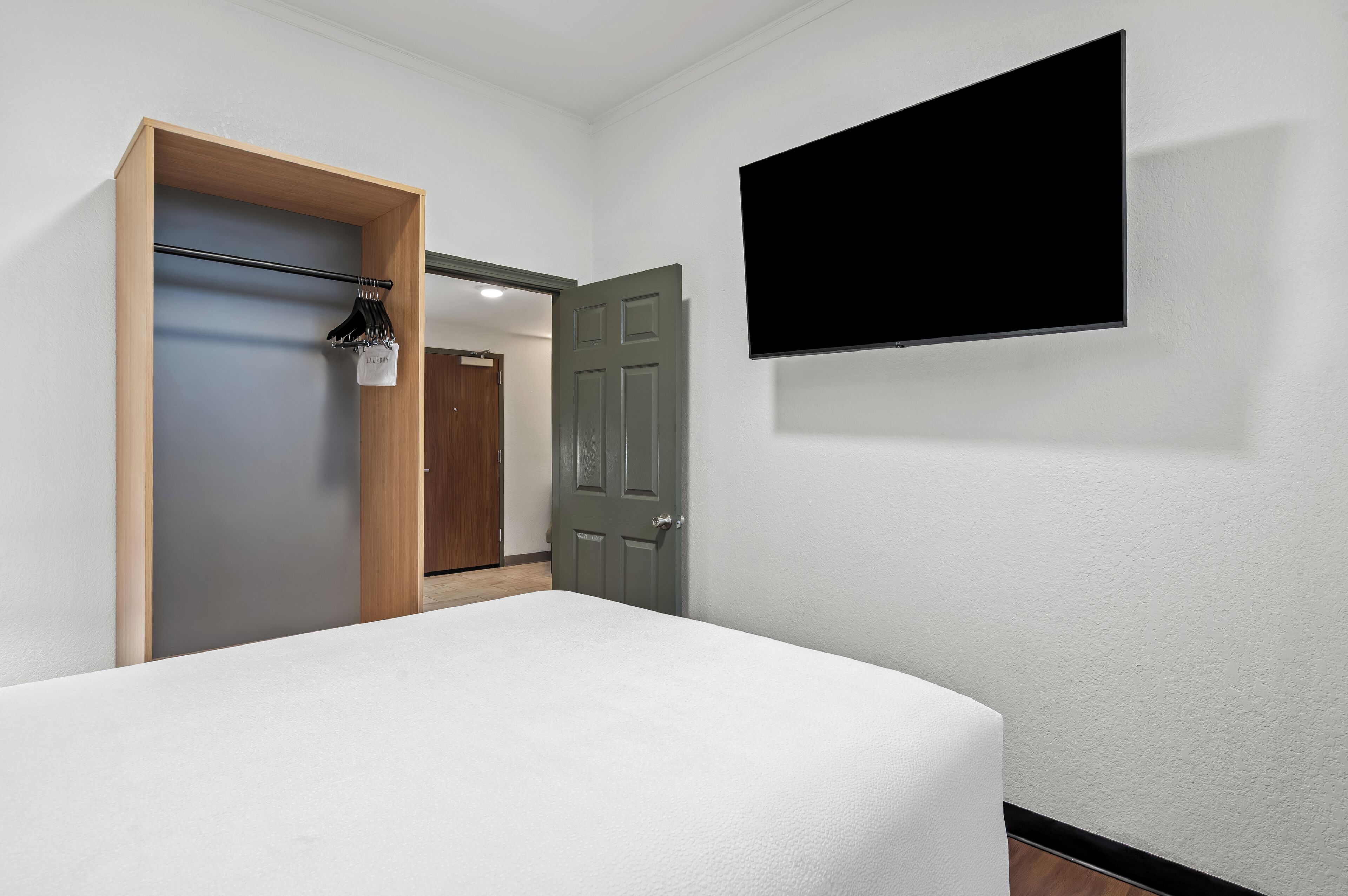 A hotel room with a bed, a wardrobe, a door, and a TV mounted on the wall.