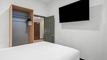 A hotel room with a bed, a wardrobe, a door, and a TV mounted on the wall.