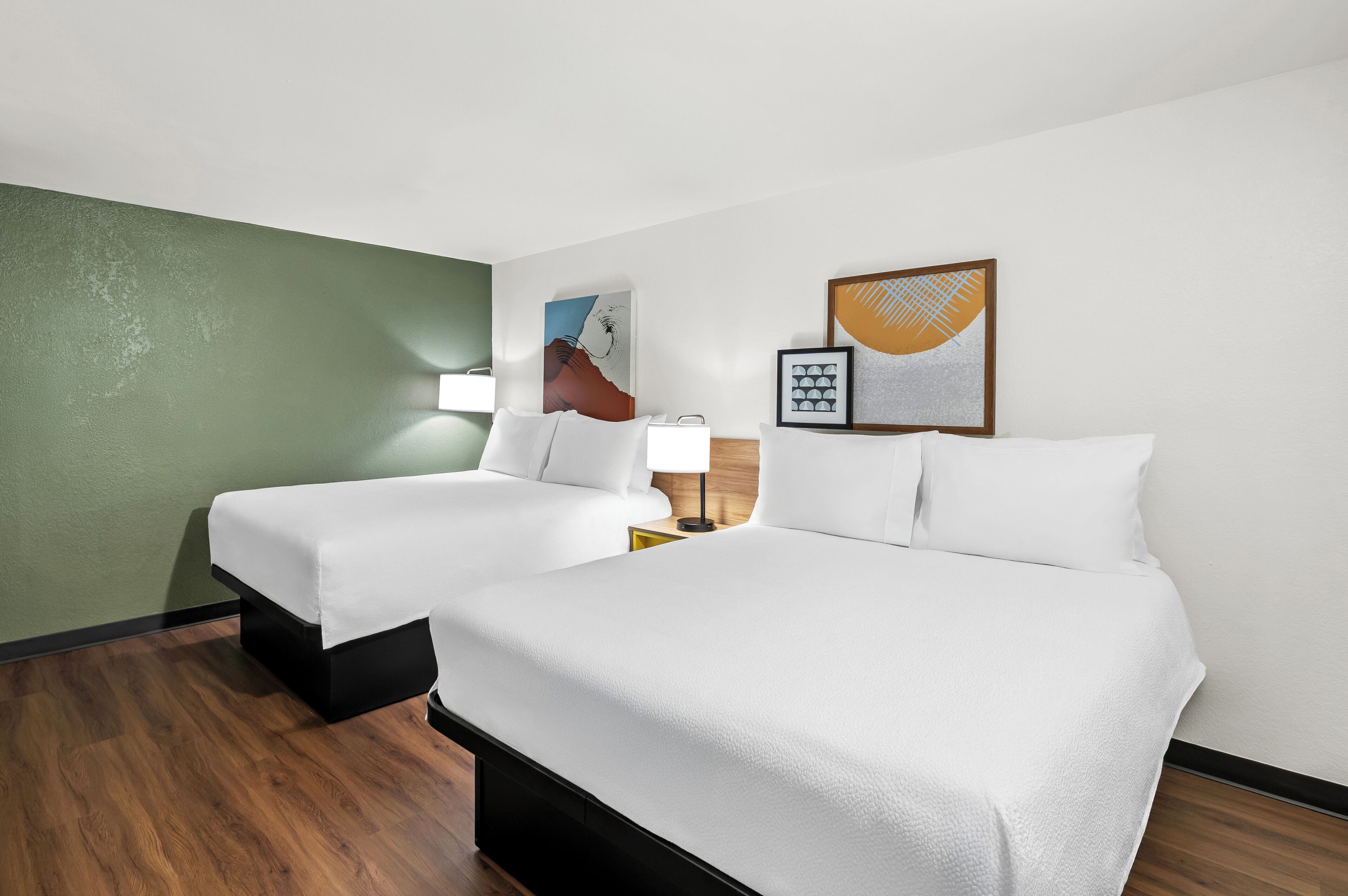 A hotel room with two beds, a green accent wall, and artwork on the walls.