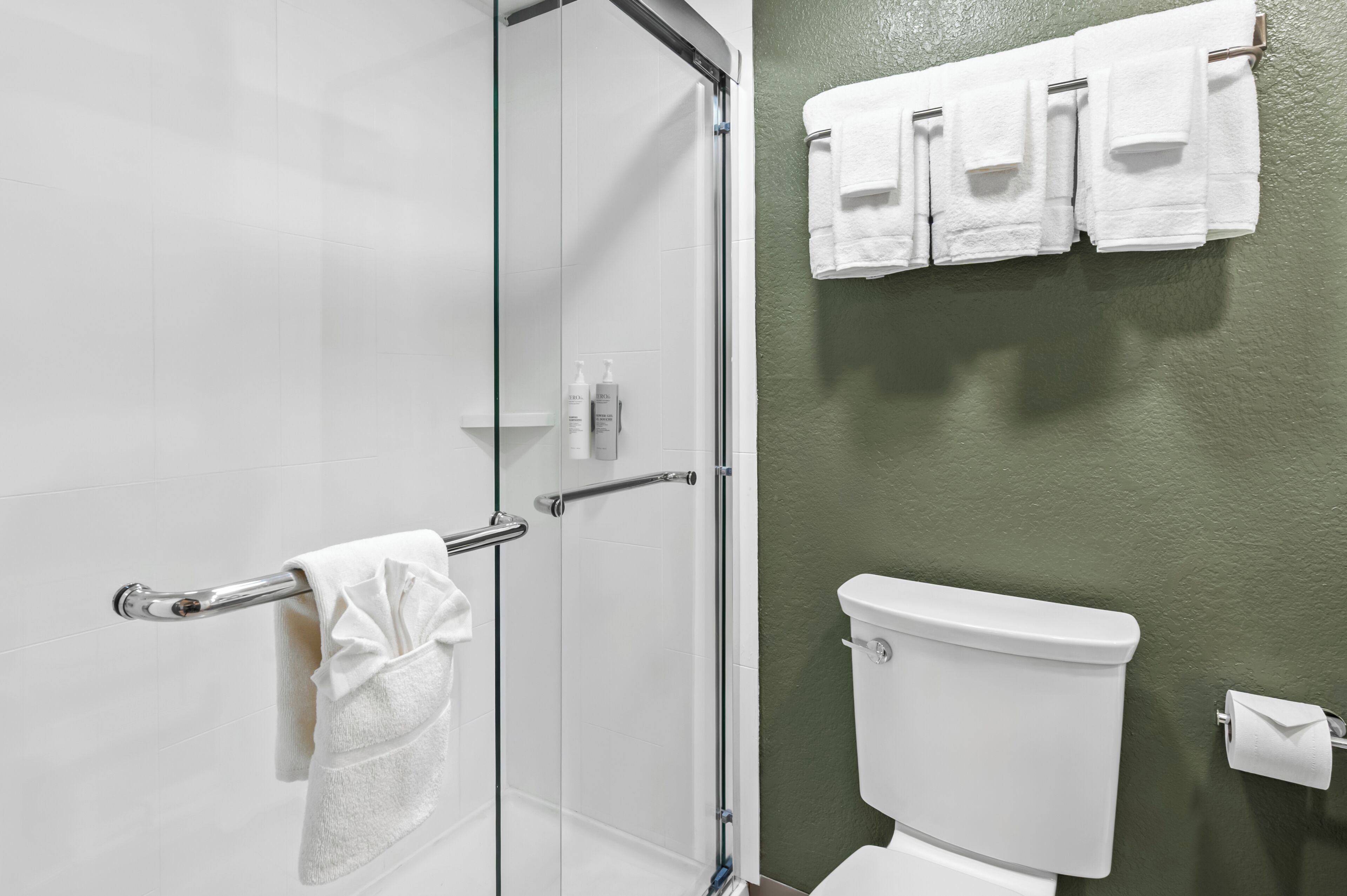A bathroom with a glass shower door, a white toilet, and a towel rack with multiple towels.