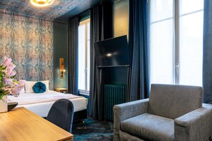 Une chambre d’hôtel avec un lit, un bureau, une chaise, une télévision et une fenêtre avec des rideaux.