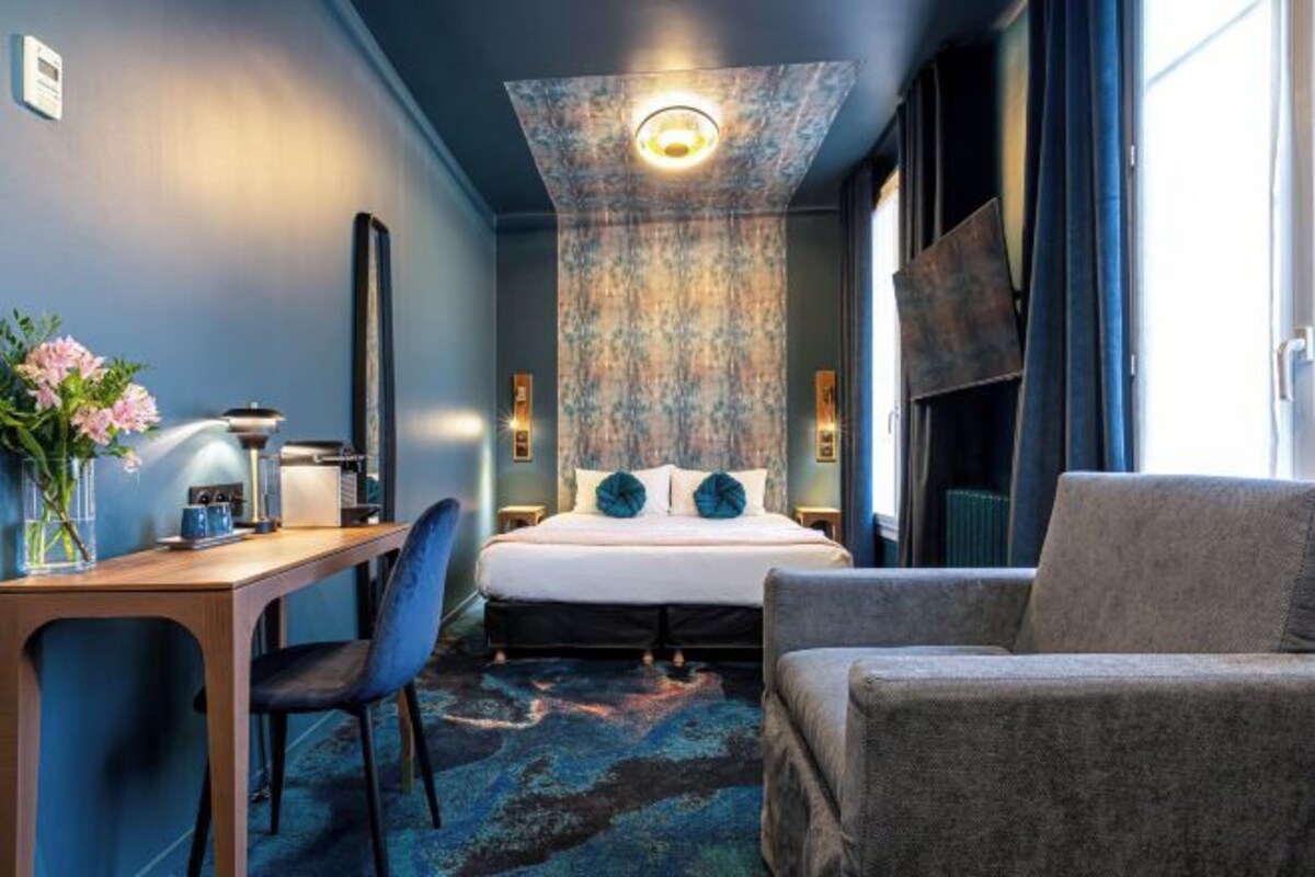 Ett modernt hotellrum med en säng, ett skrivbord, en stol och en soffa.