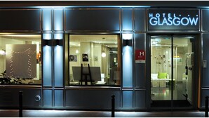 Een hotel met een moderne gevel, grote glasramen en een neonbord waarop Hotel Glasgow staat.