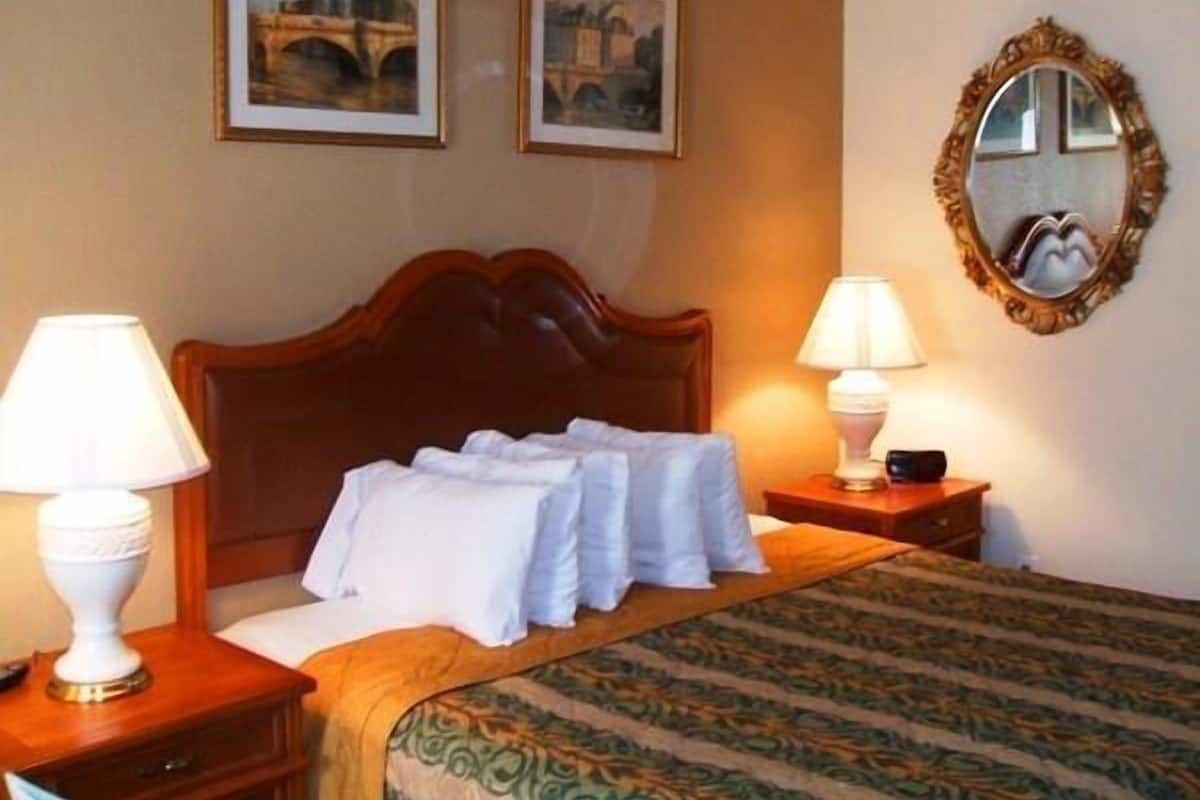 Une chambre d’hôtel avec un lit, deux lampes de chevet, un miroir et deux tableaux encadrés au mur.