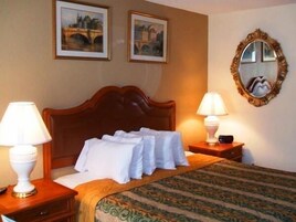 Habitación de hotel con cama, dos lámparas de noche, un espejo y dos cuadros en la pared.