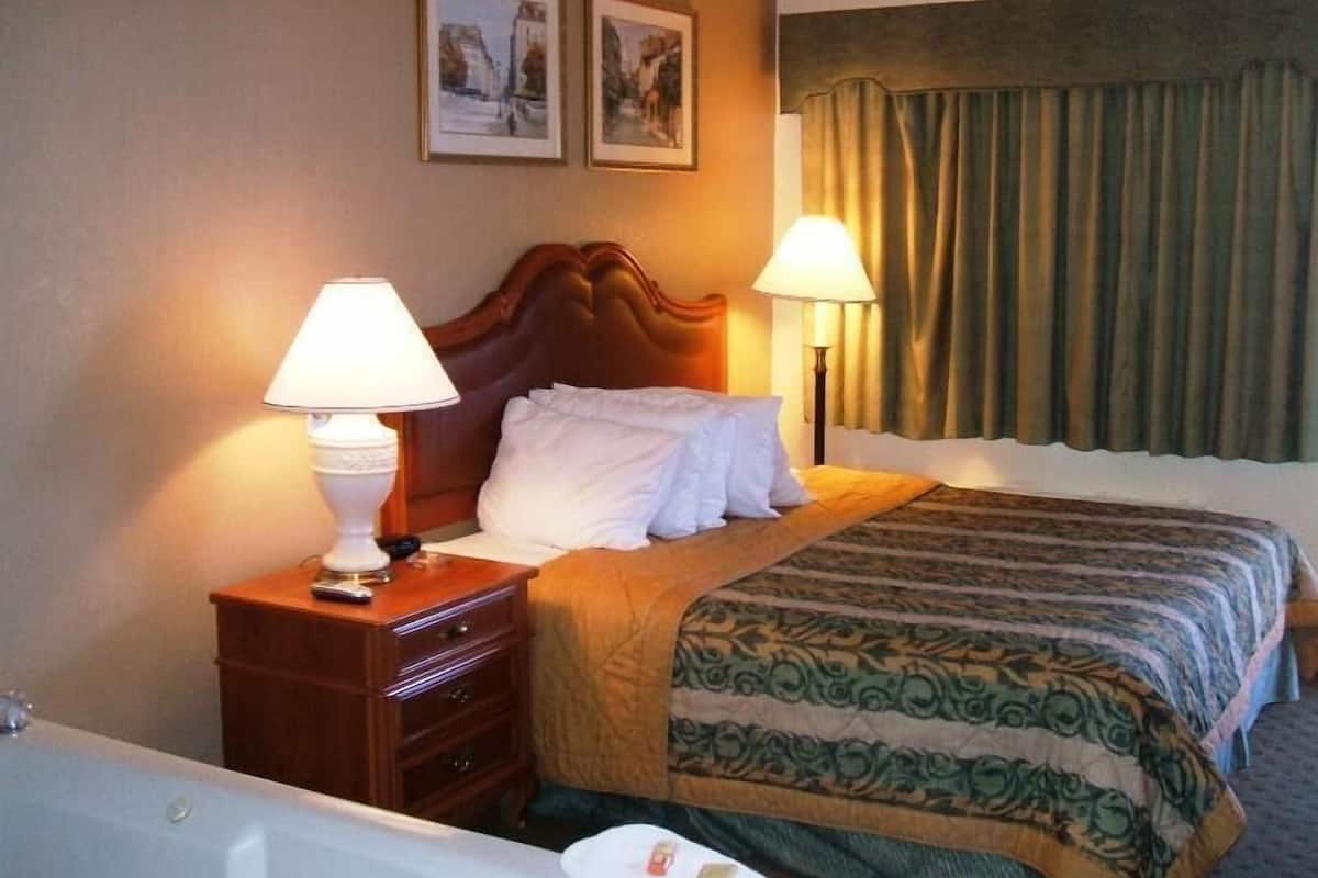 Une chambre d’hôtel comprenant un lit, deux lampes de chevet, une table de chevet en bois, une commode et une baignoire.