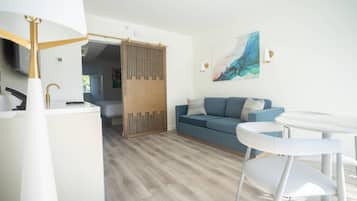 Un salon moderne avec un canapé bleu, des fauteuils blancs, une petite table blanche et une cloison en bois.
