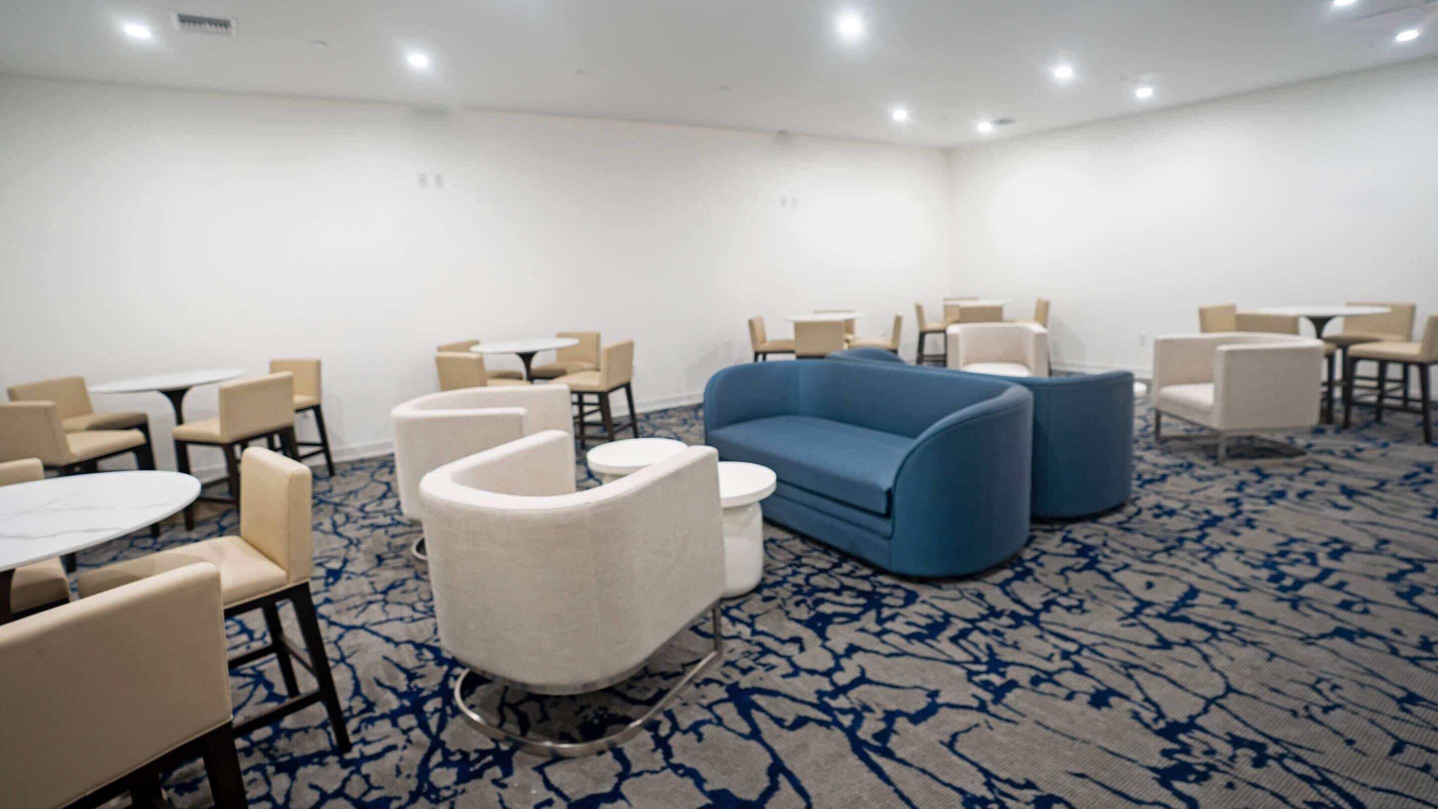 A hotel room with a blue sofa, white armchairs, and small round tables.