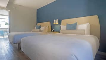 Habitación de hotel con dos camas, una mesita de noche, una lámpara y vistas al exterior.