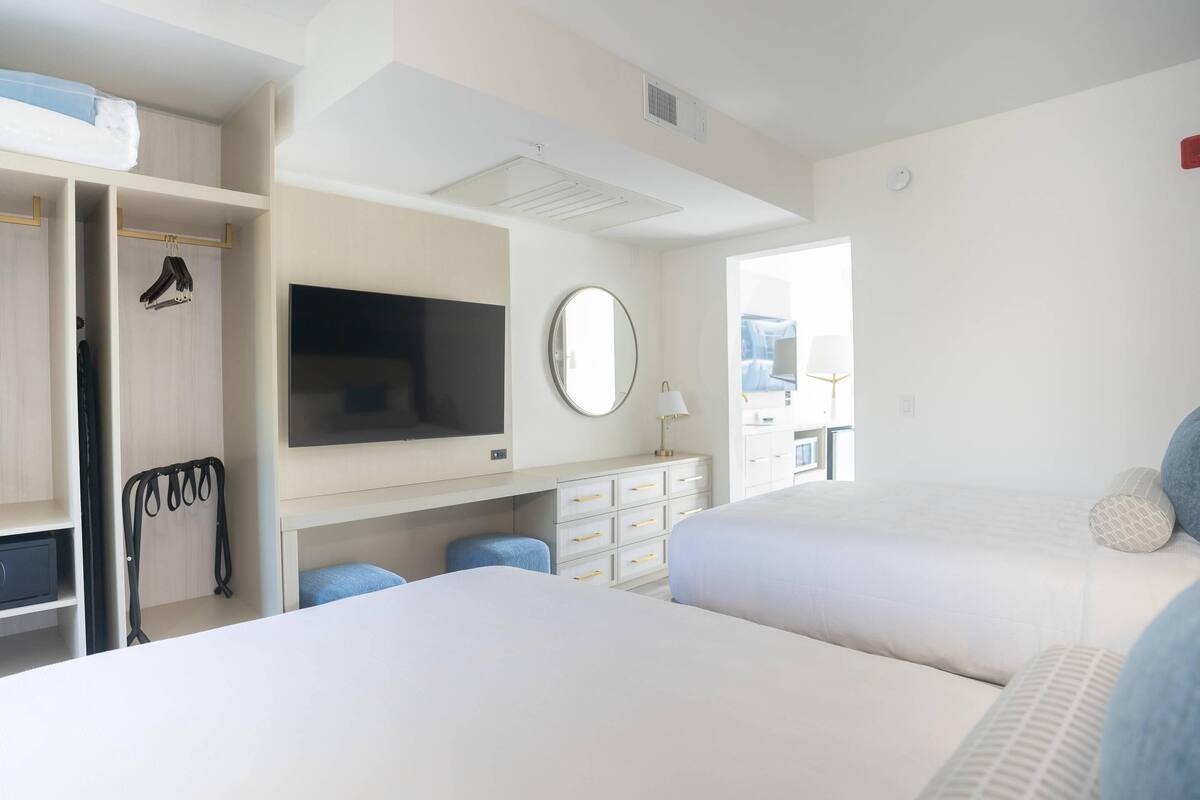 A hotel room with two beds, a TV, a mirror, a desk with drawers, and a wardrobe.