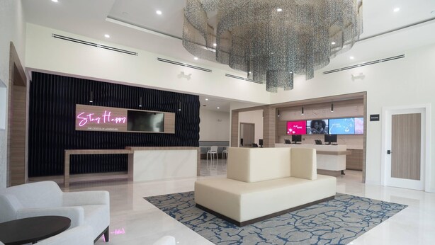 A modern hotel lobby with a reception desk, seating area, and a large chandelier.