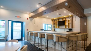 A modern bar area with a long counter, multiple stools, and a kitchen area with wooden cabinets and a TV.