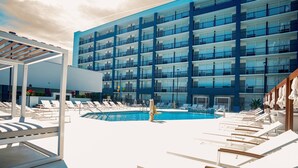 A pool area with lounge chairs and a building with multiple balconies in the background.