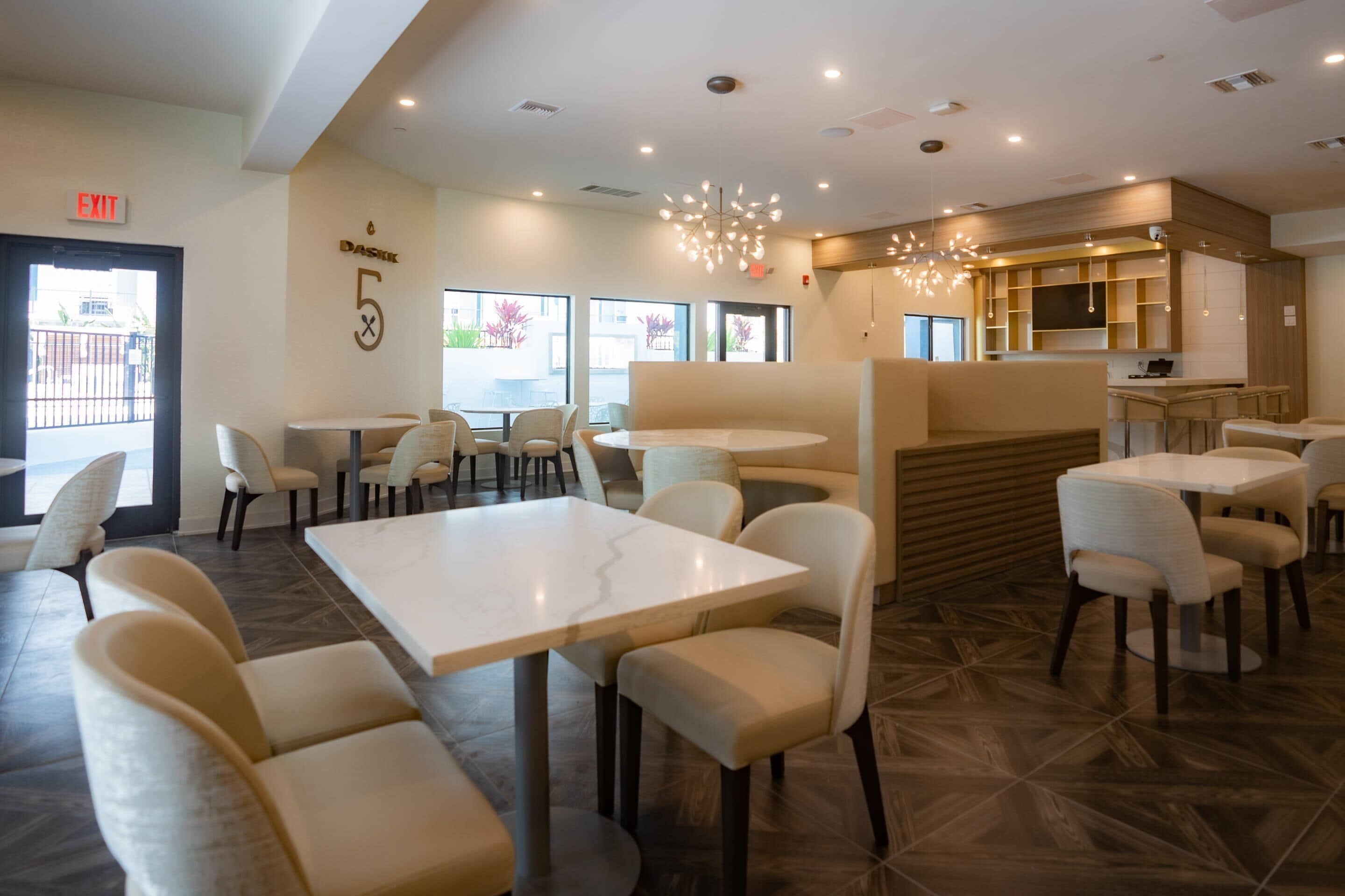 Un restaurante moderno con un área de asientos central, una barra y una cocina visible al fondo.