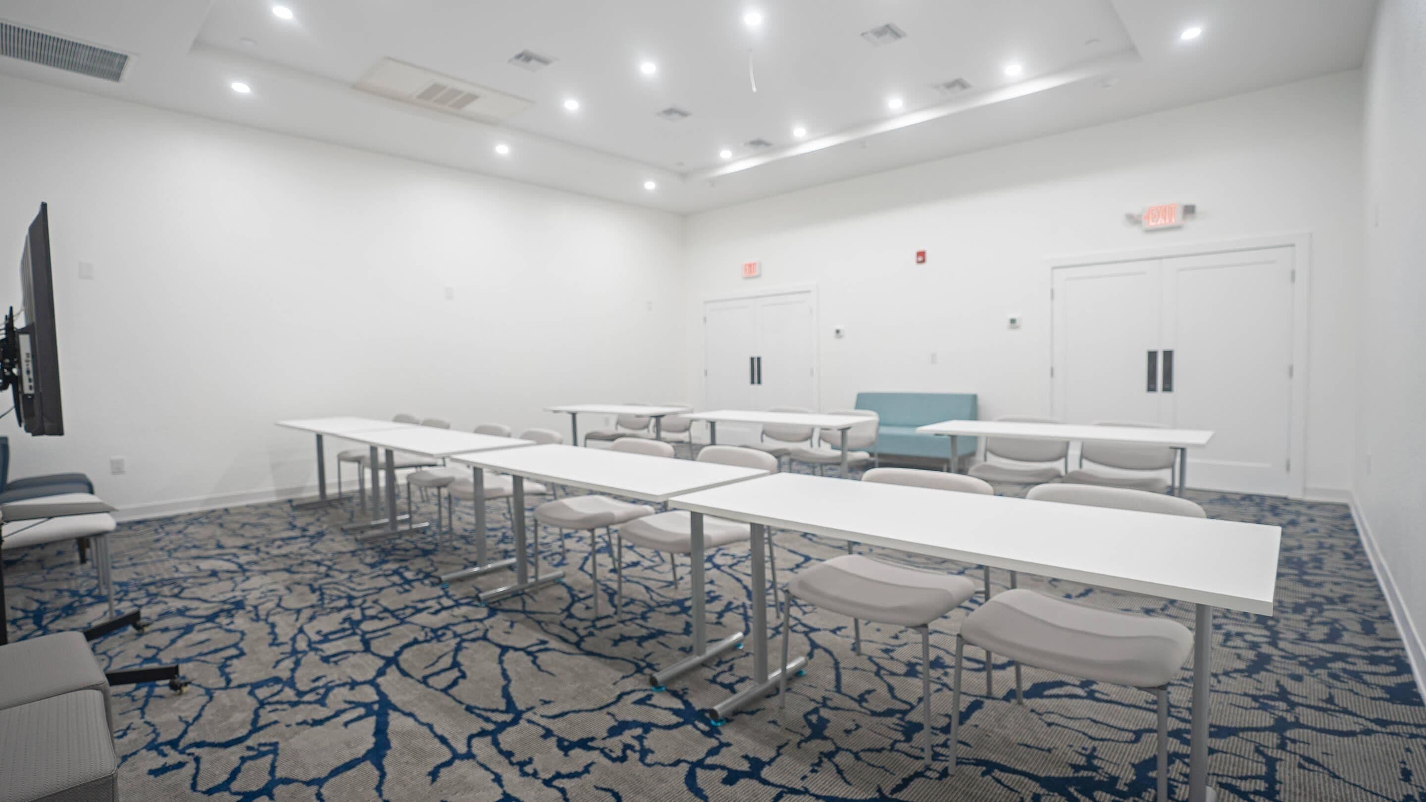 A conference room with white tables and chairs, a patterned carpet, and a blue accent wall.
