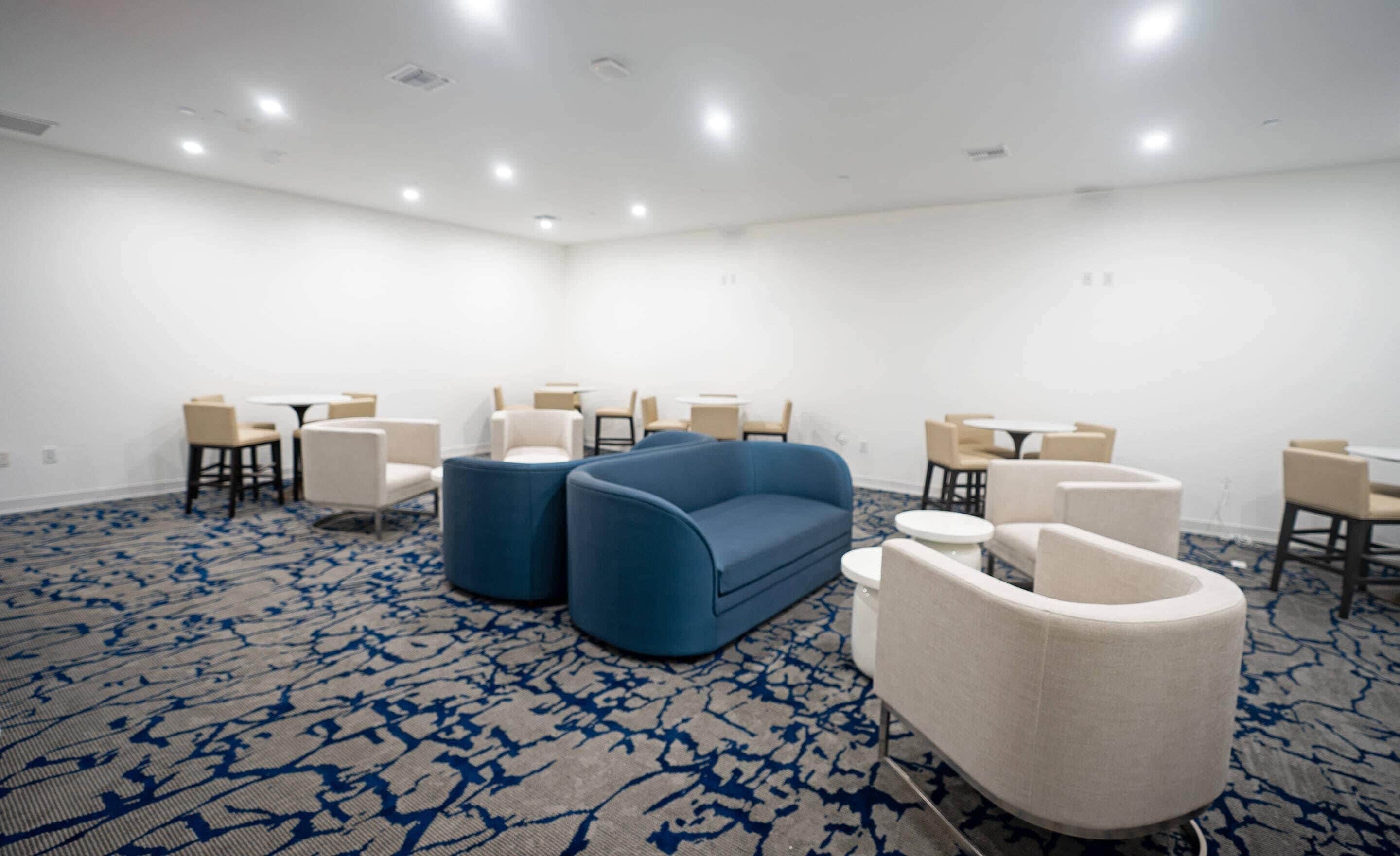 A conference room with a blue sofa, white armchairs, and small round tables.