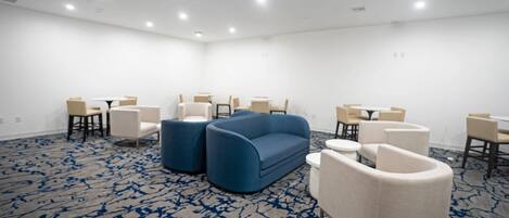 A conference room with a blue sofa, white armchairs, and small round tables.