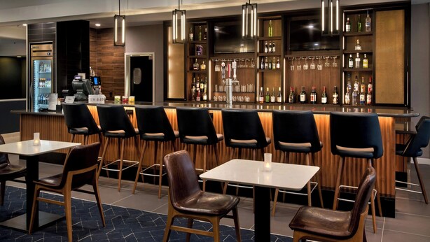 Un área de bar moderna con mostrador, taburetes y una variedad de botellas de licor.