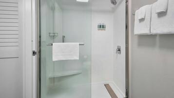 Een douche met glazen wanden, een witte handdoek aan de deurklink, een glazen plank en een handdoekhouder met twee handdoeken.