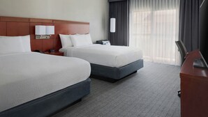 Habitación de hotel con dos camas, un escritorio, una lámpara y un ventanal con cortinas.
