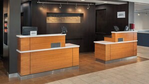 Zona de recepción moderna de hotel con mostradores de madera, un quiosco de registro digital y un cartel con el nombre del hotel.