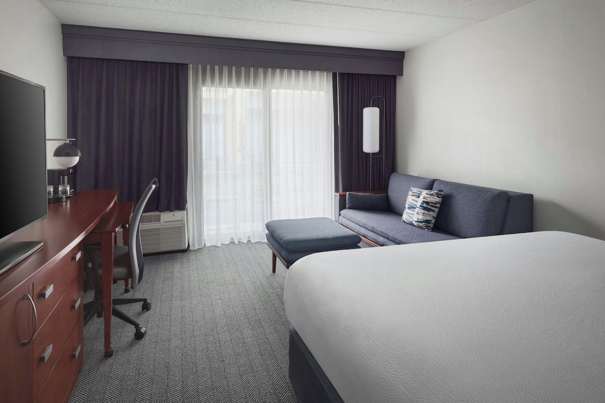 A hotel room with a large bed, a desk with a chair, a sofa, and a TV.