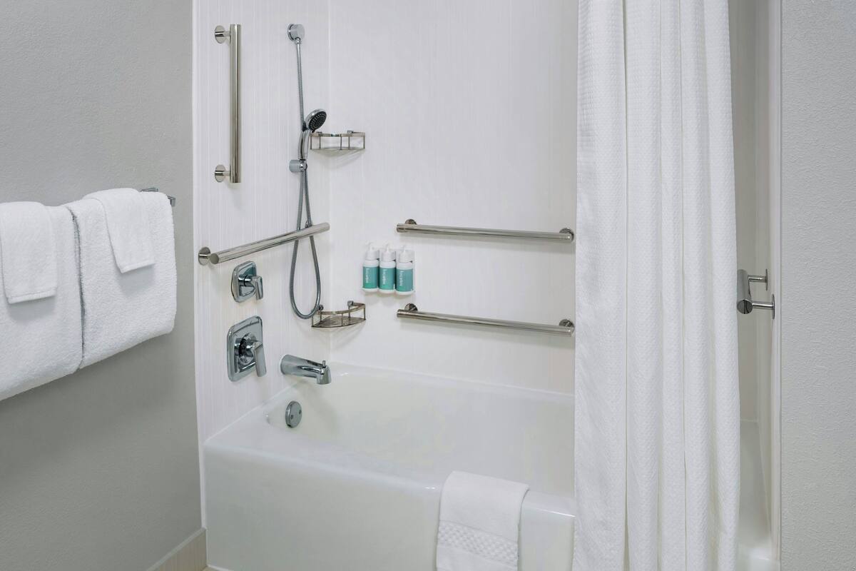 A bathroom with a bathtub, grab bars, a showerhead, and a towel rack.