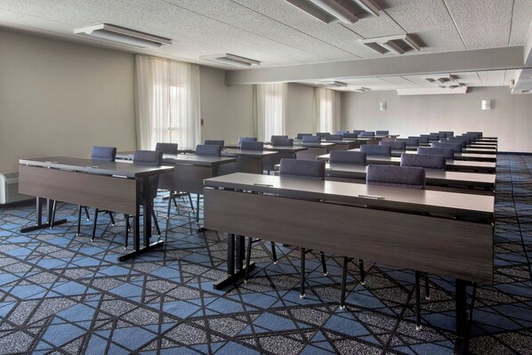 Un salón de conferencias con mesas largas, sillas y una alfombra estampada.