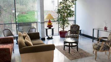 Una habitación amplia con un gran ventanal, un sofá, una silla, una mesita y una planta en maceta.
