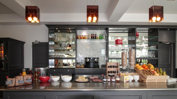 A modern kitchen with a central island, glass-fronted cabinets, and a variety of food items and condiments. - ibis Périgueux Centre (Périgueux)