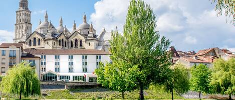 Un edificio histórico con múltiples cúpulas y una torre, ubicado junto a un río tranquilo y abundante vegetación.