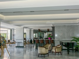 Um hall amplo com piso de mármore, cadeiras de madeira, um piano e um espaço de refeições com mesas e cadeiras.