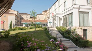 A hotel with a central courtyard, a staircase leading to the entrance, and a flag on the building. - ibis Périgueux Centre (Périgueux)