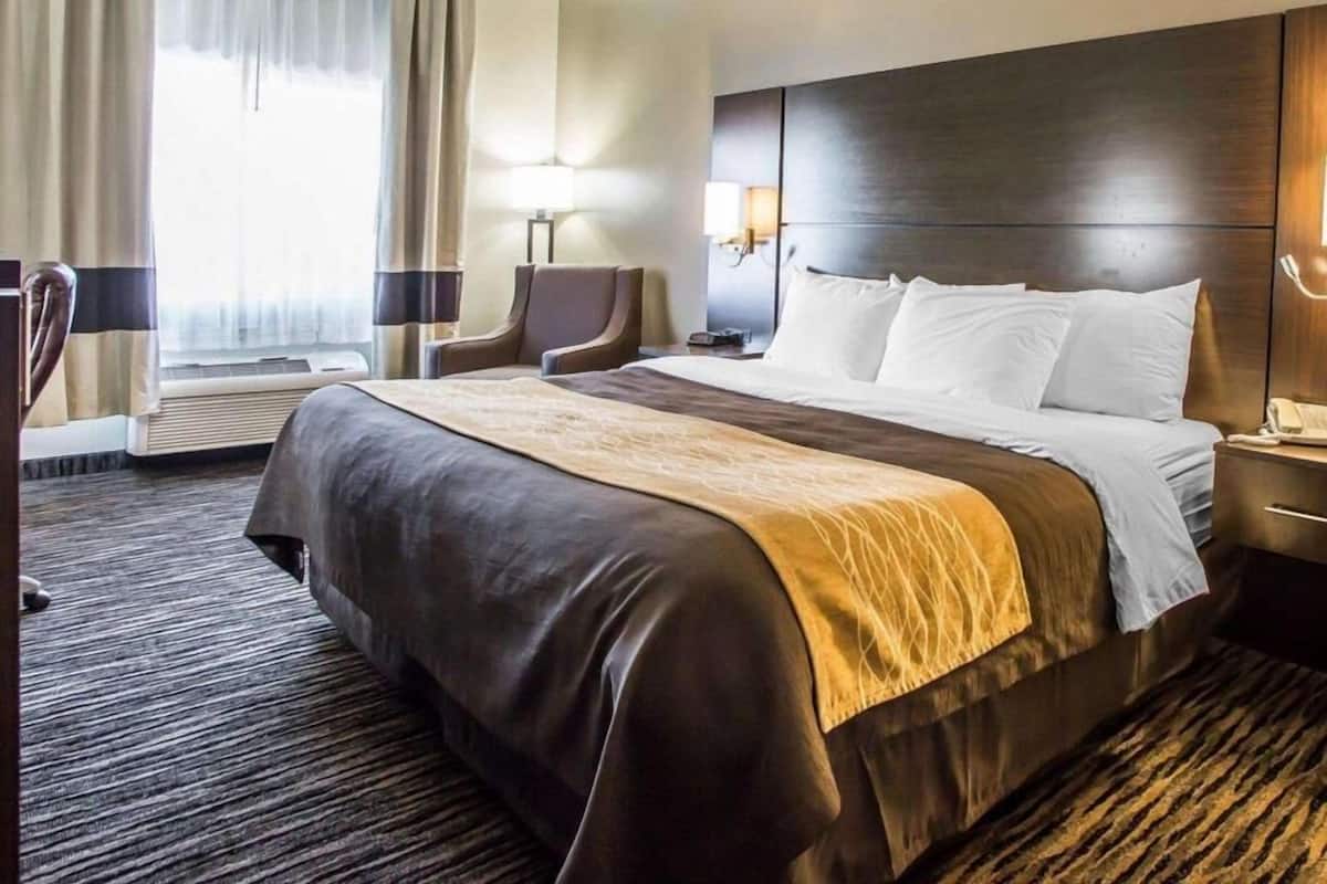A hotel room with a large bed, a desk, a chair, a lamp, and a window with curtains.