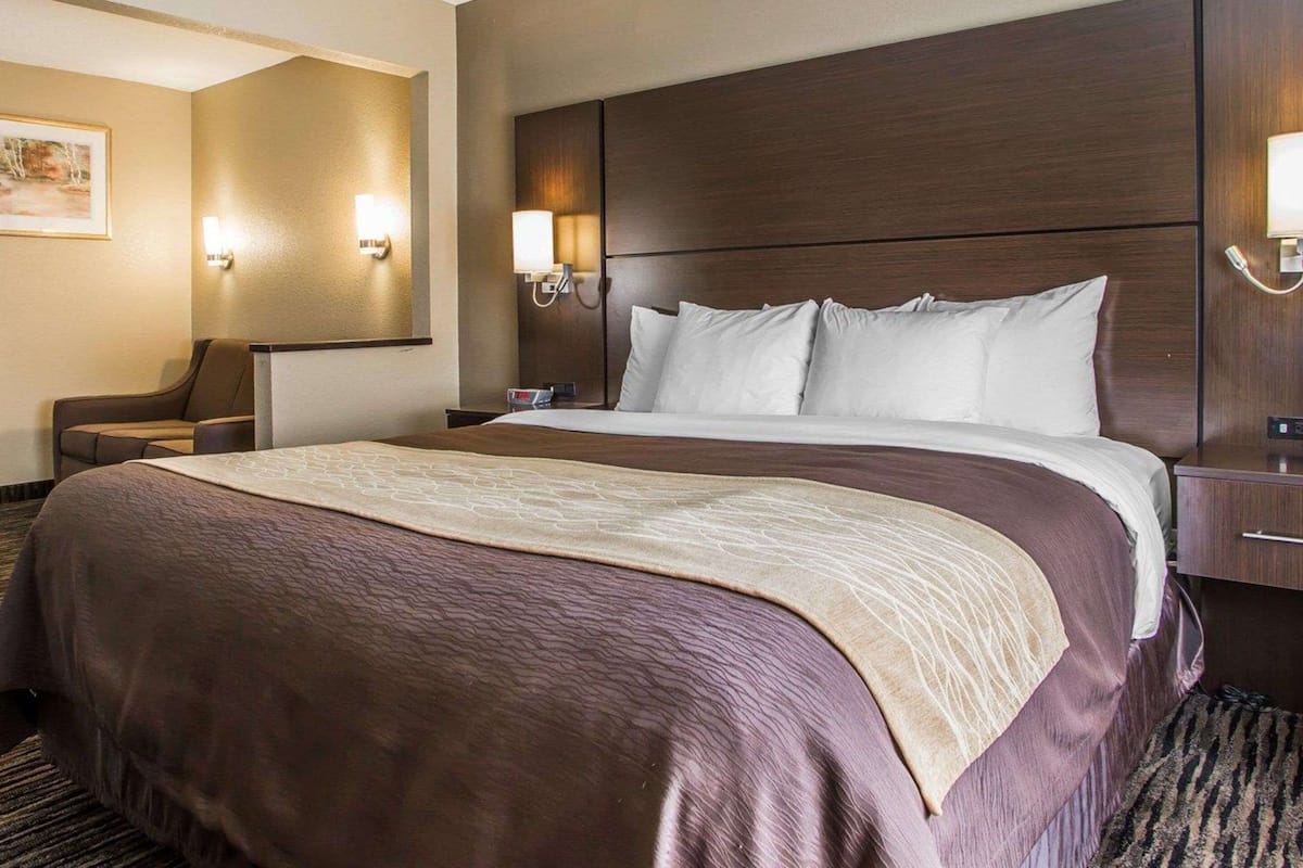 A hotel room with a large bed, two bedside tables, a nightstand, a chair, and wall-mounted lamps.